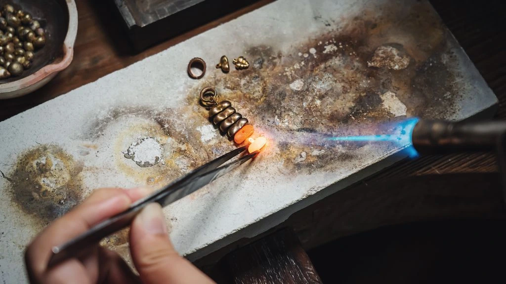 A goldsmith's hands shaping a brass signet at the Lyon atelier bench, in warm golden-hour light.