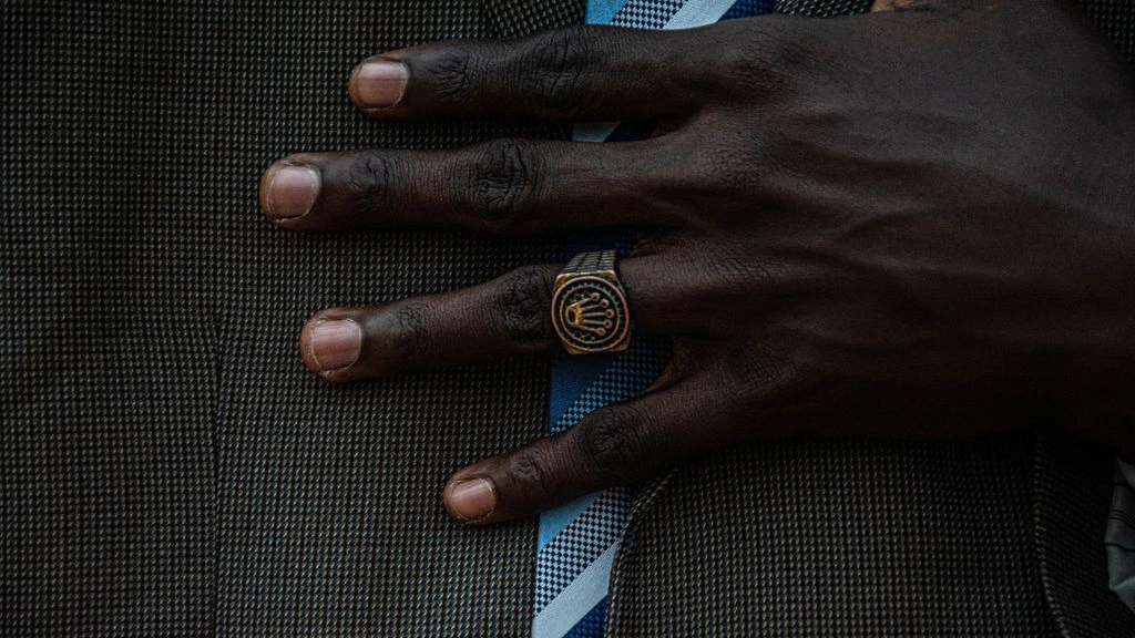 A hand wearing an architectural brass cuff, set against a Lyon stone wall.